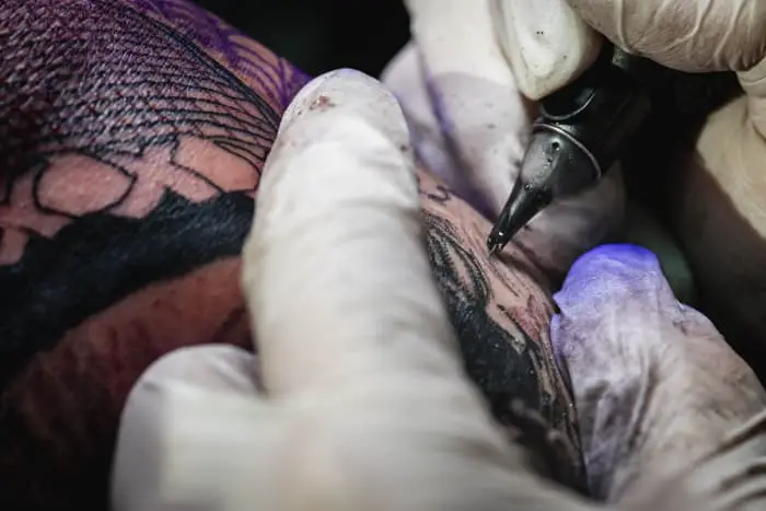 Closeup of tattoo artist's hands using ink on person's skin.