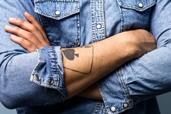 An Ace of Spades tattoo on a man's forearm, partially hidden by his shirt sleeve -- an Ace of Spades tattoo meaning has lots of room for interpretation, based on overall context and the wearer.