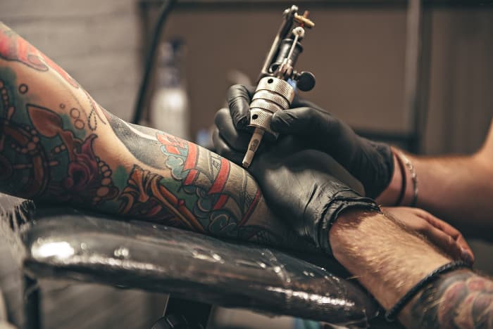 Tattoo artist working on client's arm.