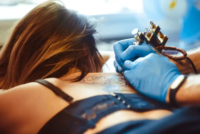 A tattoo artist working on the back of a woman's shoulder.