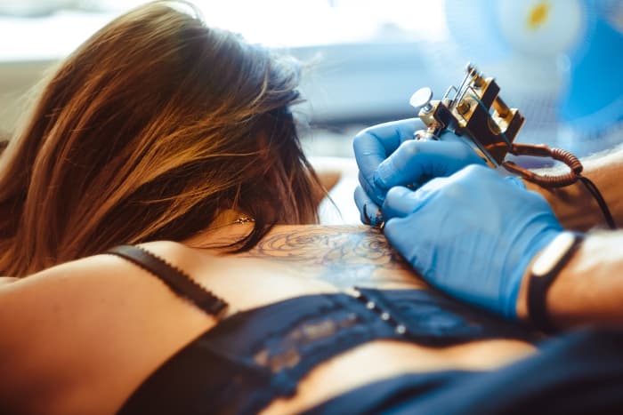 A tattoo artist working on the back of a woman's shoulder.