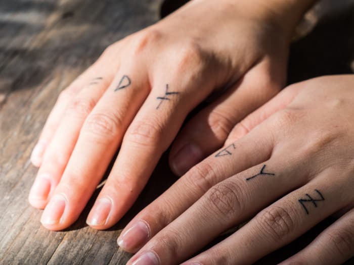 Letters in black ink tattooed on a woman's fingers.