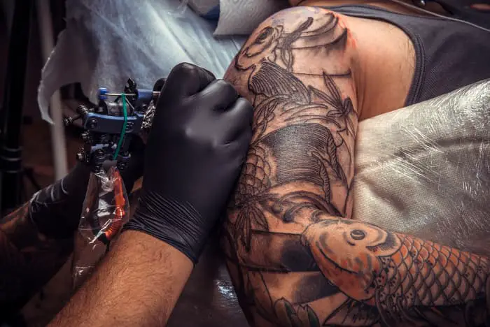A tattooist working on a man's upper arm.