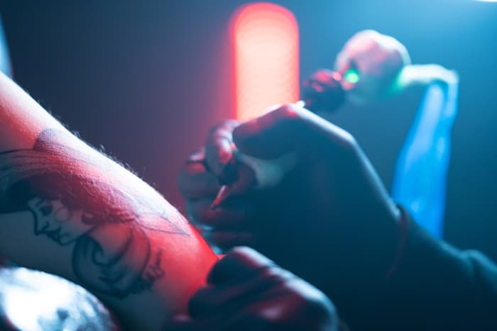 Closeup of a tattooist's black gloved hands working on a client's arm.