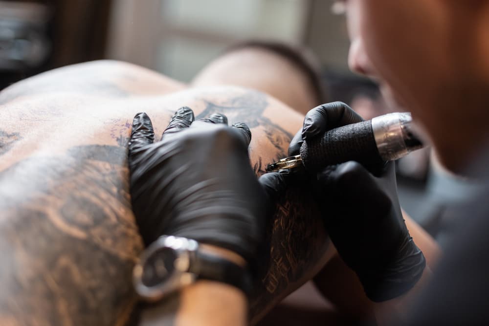 Closeup of a tattooist working on a client's back.