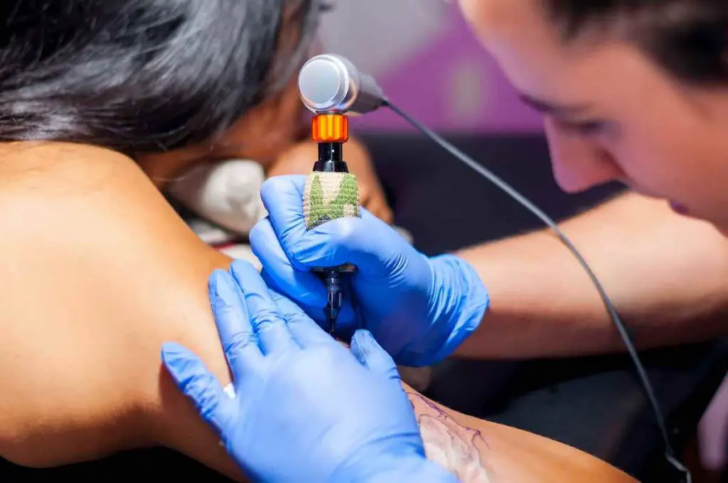 A tattoo artist working on a woman's upper arm.