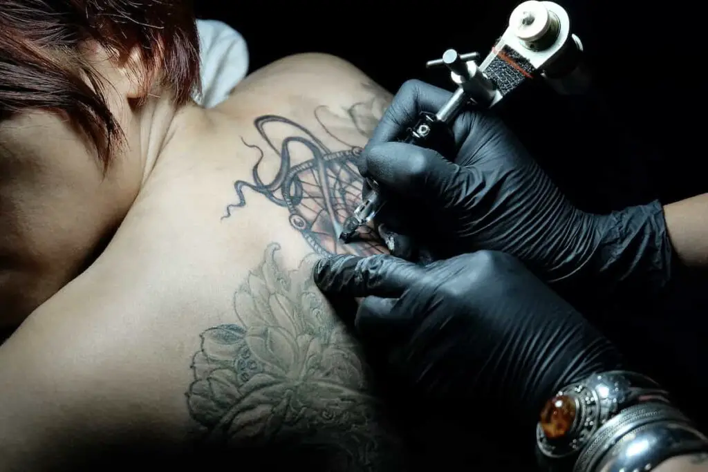 A tattoo artist working on a woman's upper back.