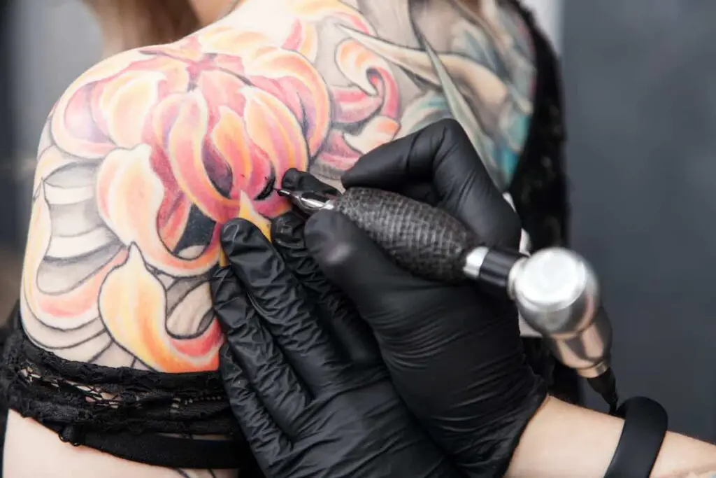 A tattooist using a tattoo gun on the back of a woman's shoulder.