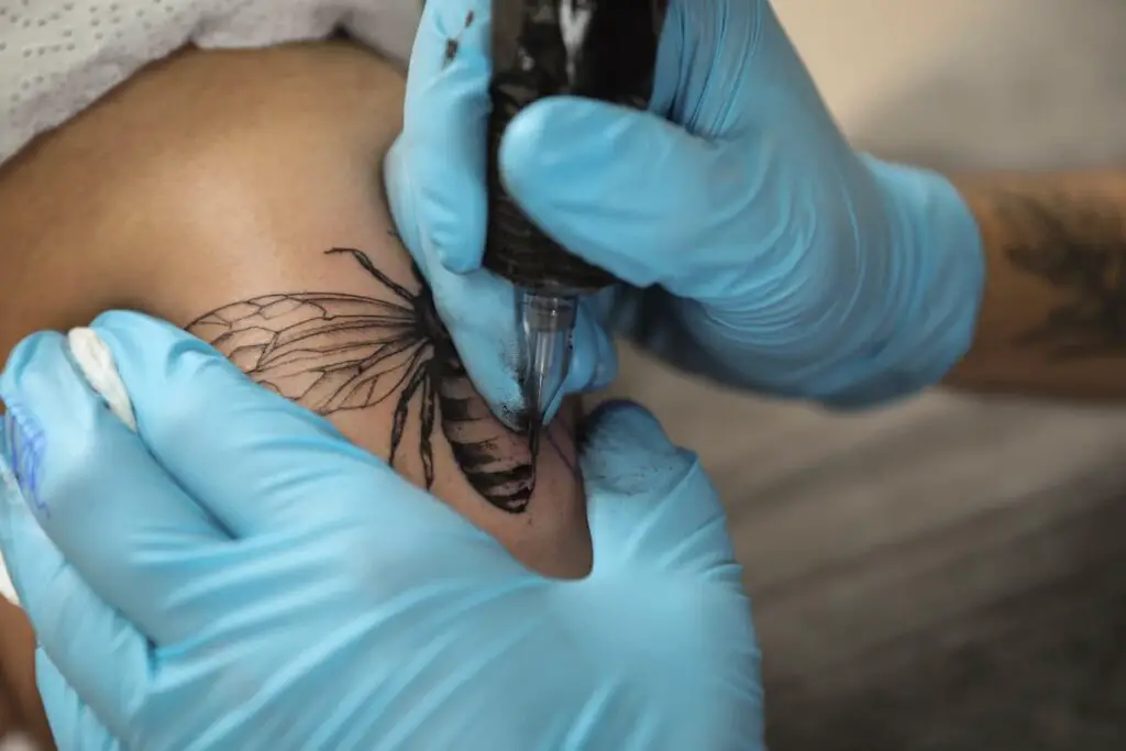 Tattoo artist working on tattoo with a bee in the design.