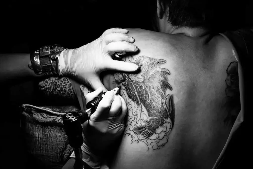 A black and white photo of a tattoo artist working on a back shoulder canvas.