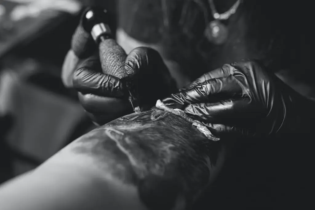 A tattoo artist working on a dark tattoo of a bird resembling a raven.