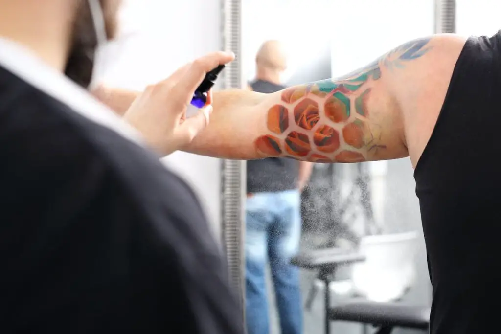 Tattoo artist applying disinfectant spray to a new tattoo.