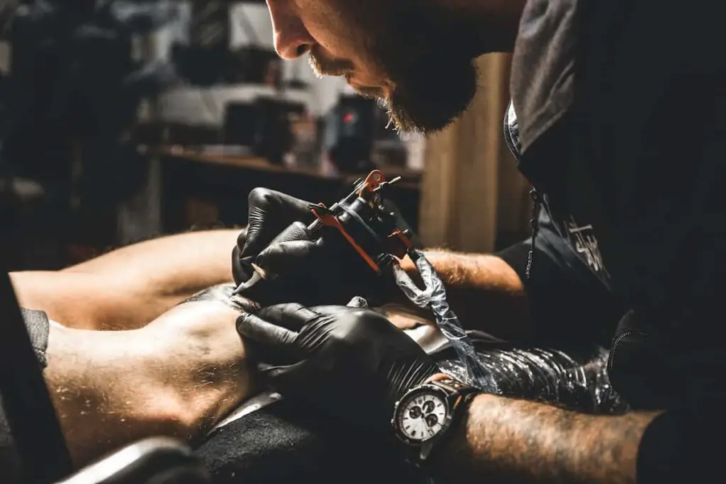 A tattoo artist working on a client's leg.