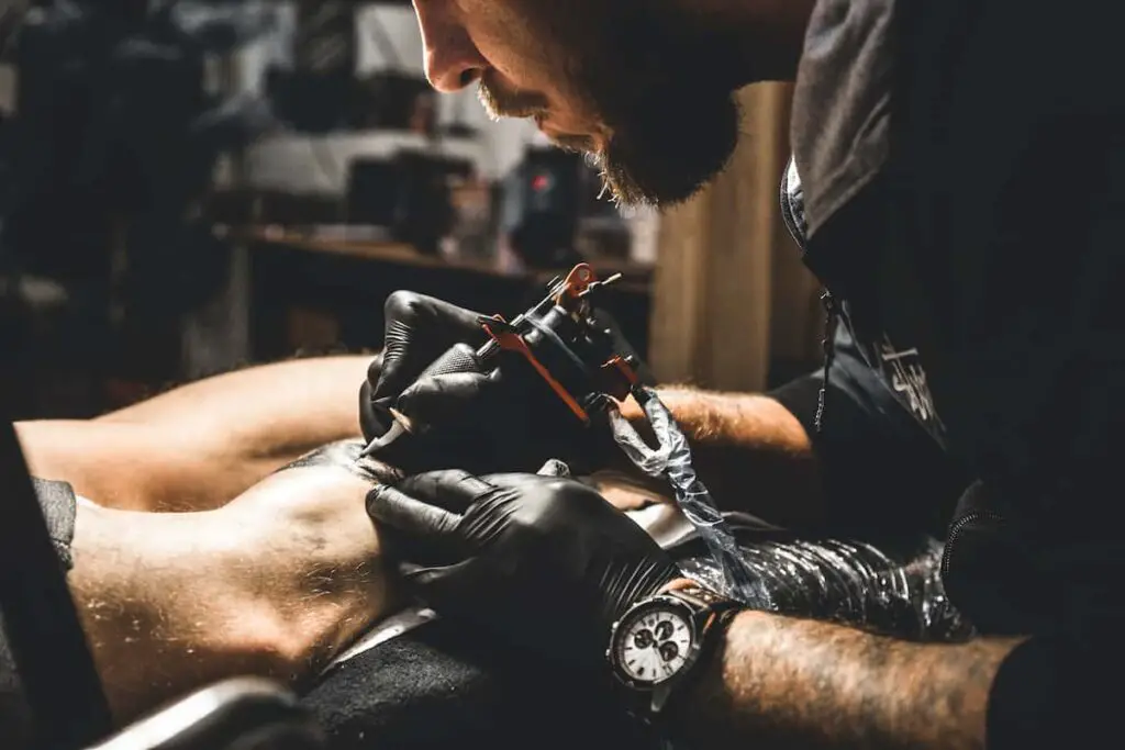 Tattoo artist working on client's leg.