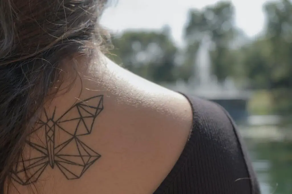 A geometric butterfly tattoo on a woman's upper back and shoulder area.