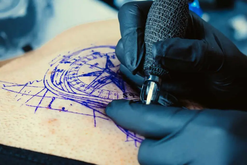 A tattoo artist working on a compass tattoo.
