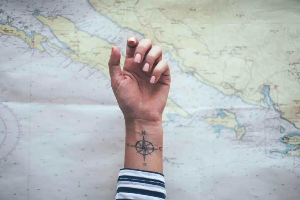 Woman with a compass tattoo on her inner wrist and a world map in the background.