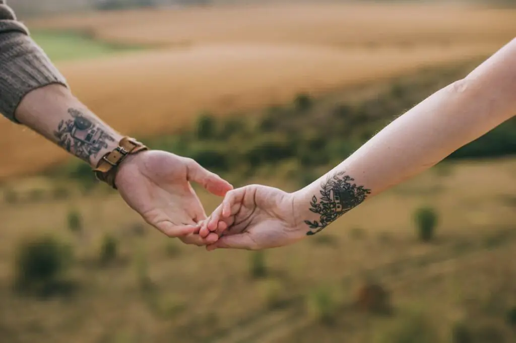 Couple holding hands and showing matching tattoos near their wrists.