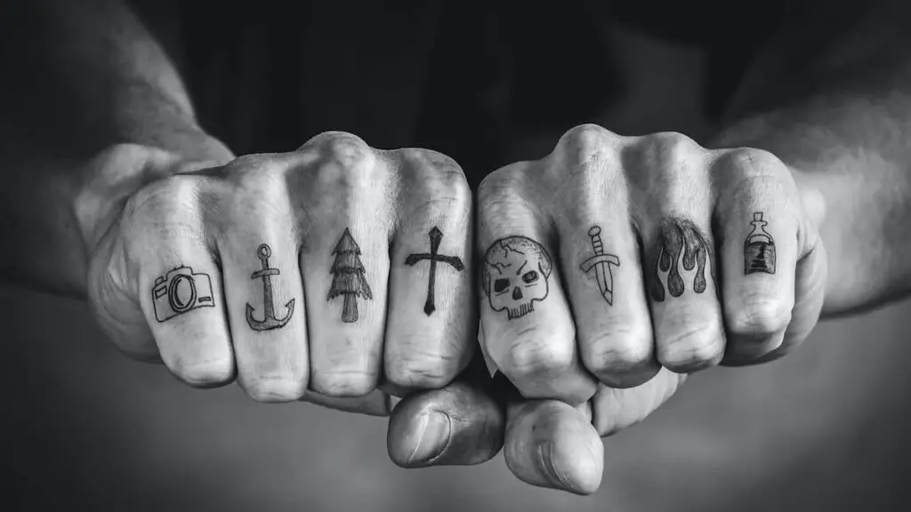 Black and white image of tattoos on a man's fingers, one of them an anchor.