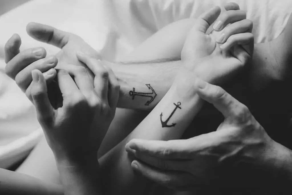 Man and a woman's wrists with anchor tattoos on them.