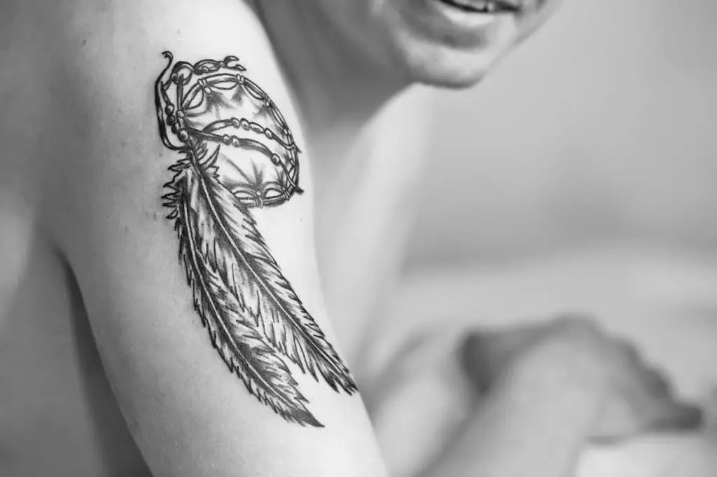 A man with a tattoo of a dreamcatcher that has feathers. Feather tattoo meanings depend on the context of the tattoo.