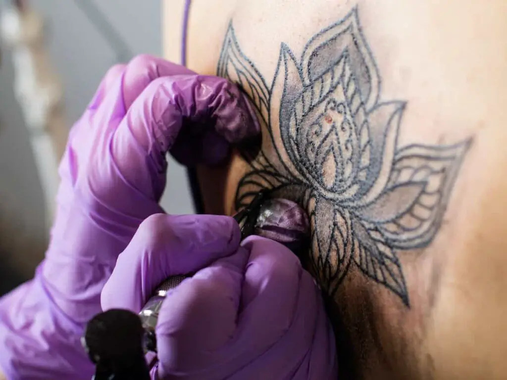 A tattoo artist working on a lotus flower tattoo.