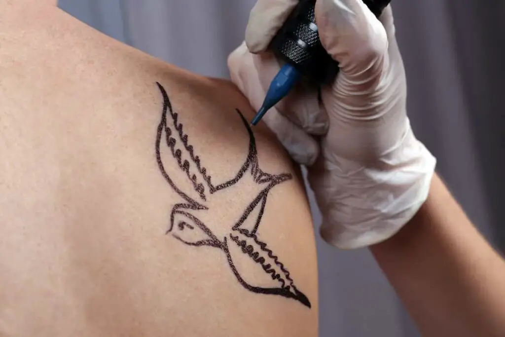 A tattoo artist creating a swallow tattoo on a woman's shoulder.