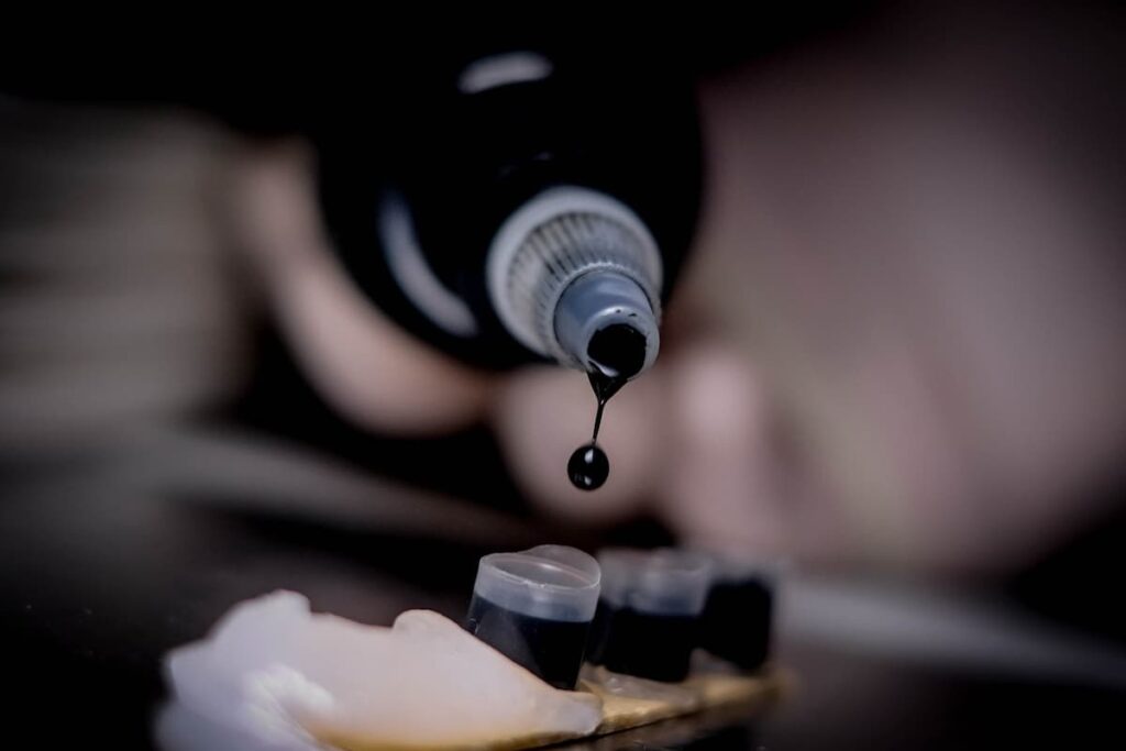 Person pouring black tattoo ink into small plastic cups.