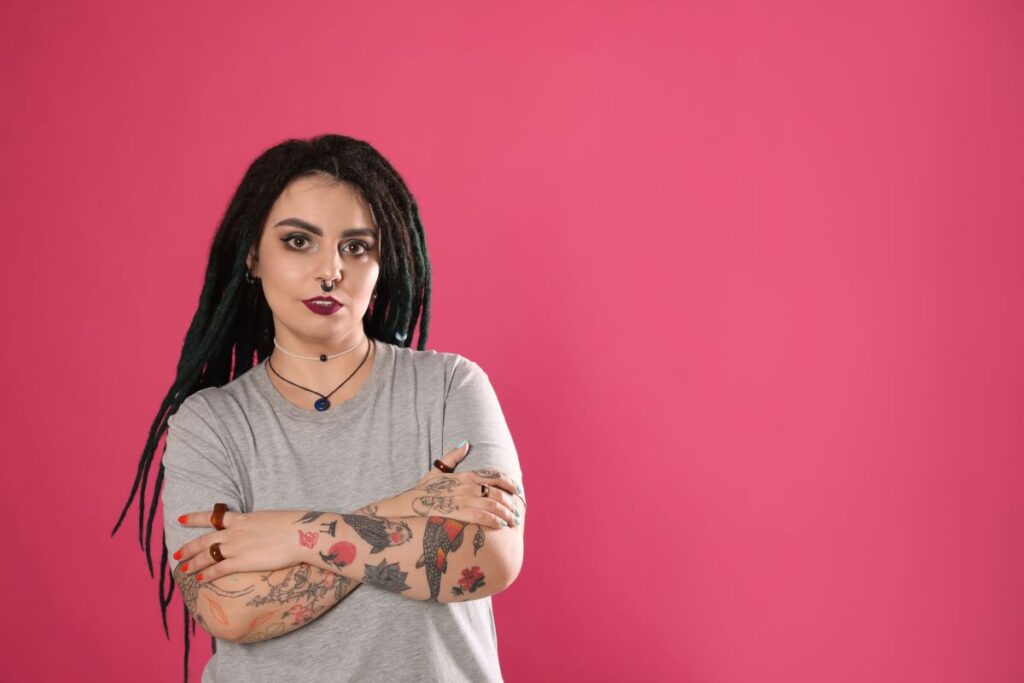 Woman in front of a pink background with a koi fish tattoo on her arm.