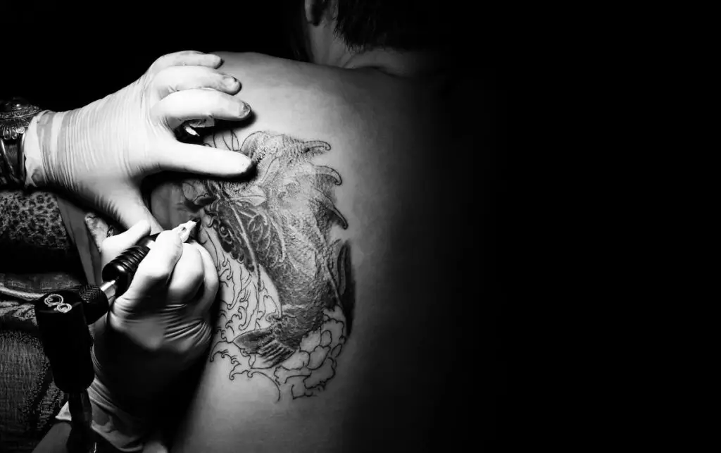 Tattoo artist creating a koi fish tattoo on a woman's back. Discover koi fish tattoo meanings.