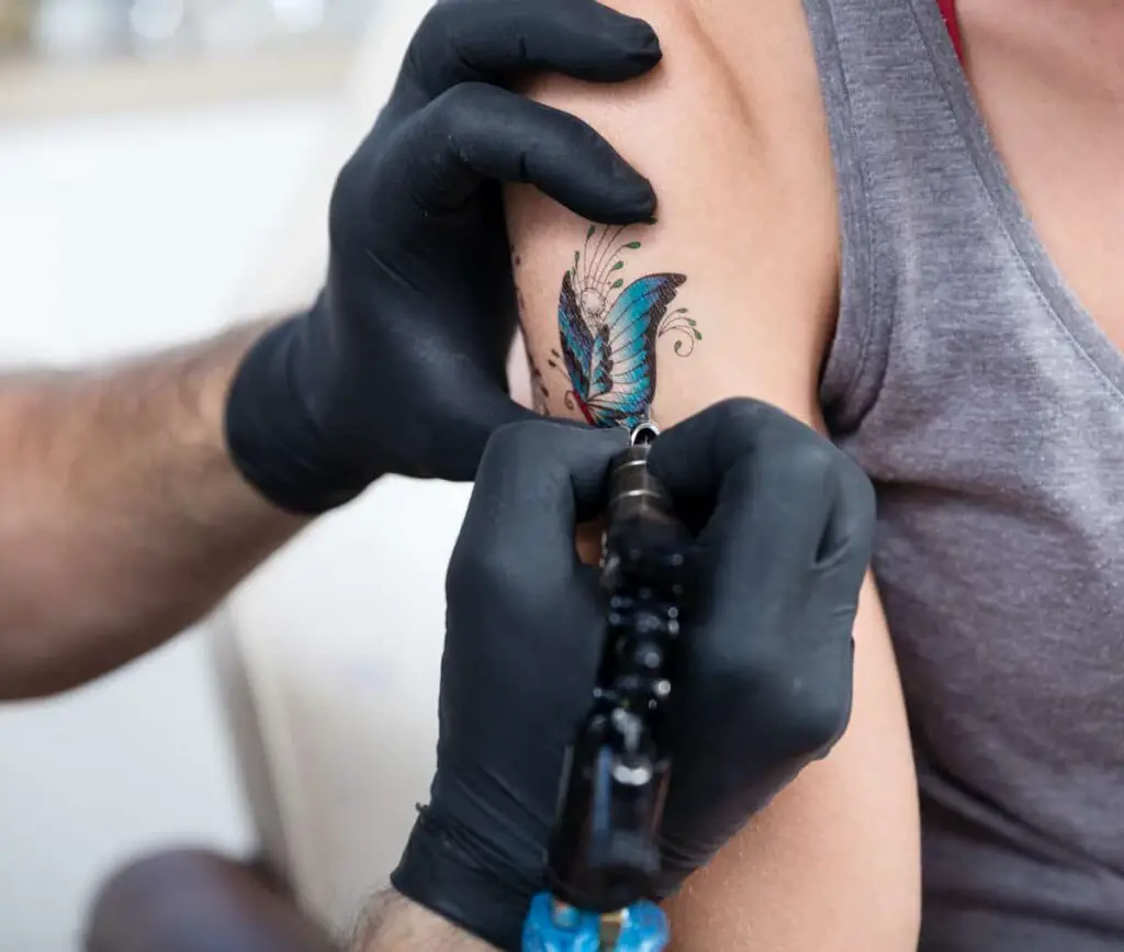 A tattoo artist working on a blue butterfly tattoo.