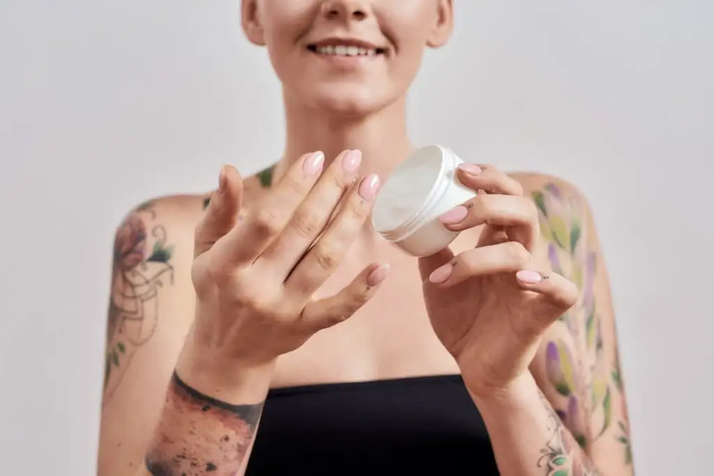 Woman with tattoo holding jar of ointment.