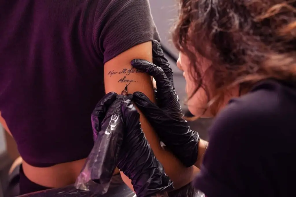 A tattoo artist working on a script tattoo.