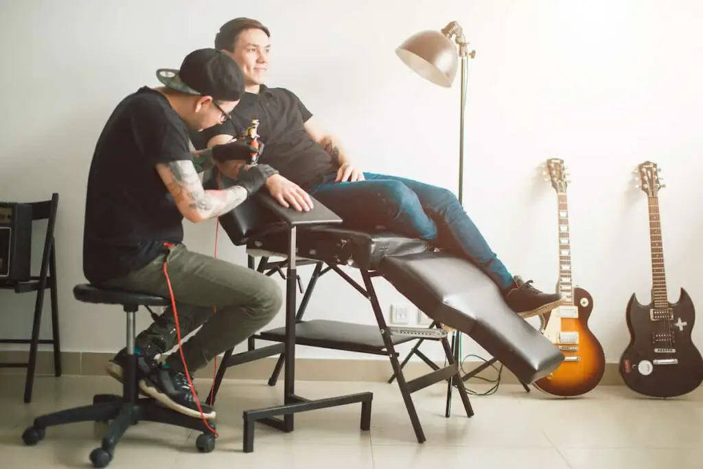 A tattoo artist seated while working on a tattoo. Tattoo artist chairs.