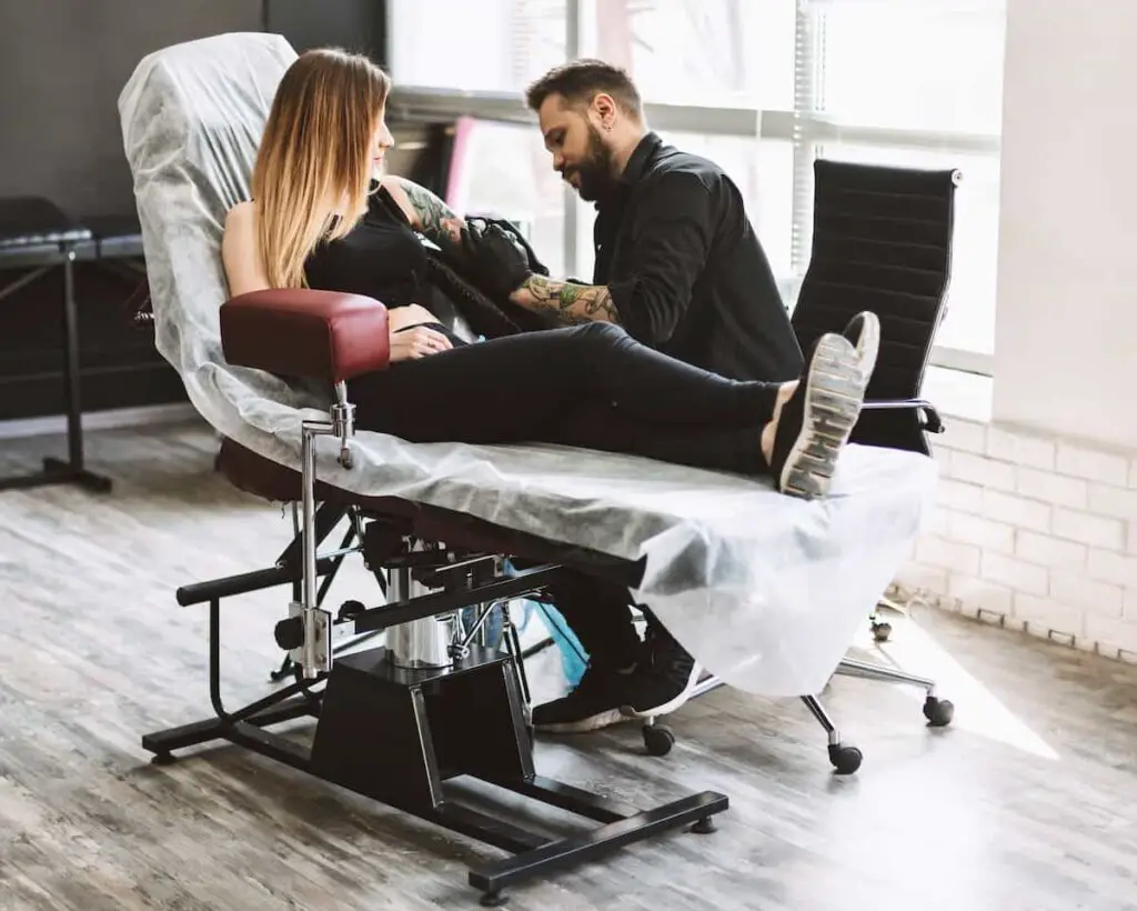 A tattoo artist seated on a high-backed rolling chair while working on a client.