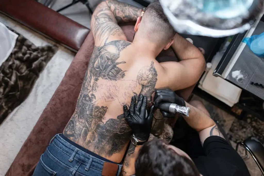A tattoo artist working a client's back under bright light.