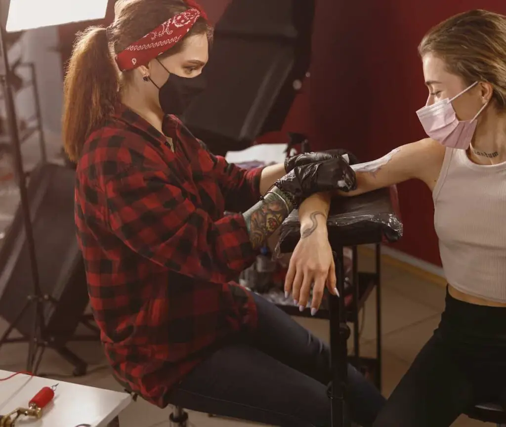 A tattoo artist seated on a padded stool while working on a client's tattoo.