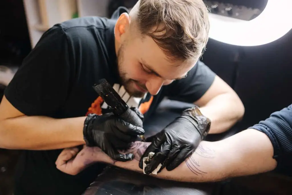 A tattoo artist using a ring light while working on a client's arm.