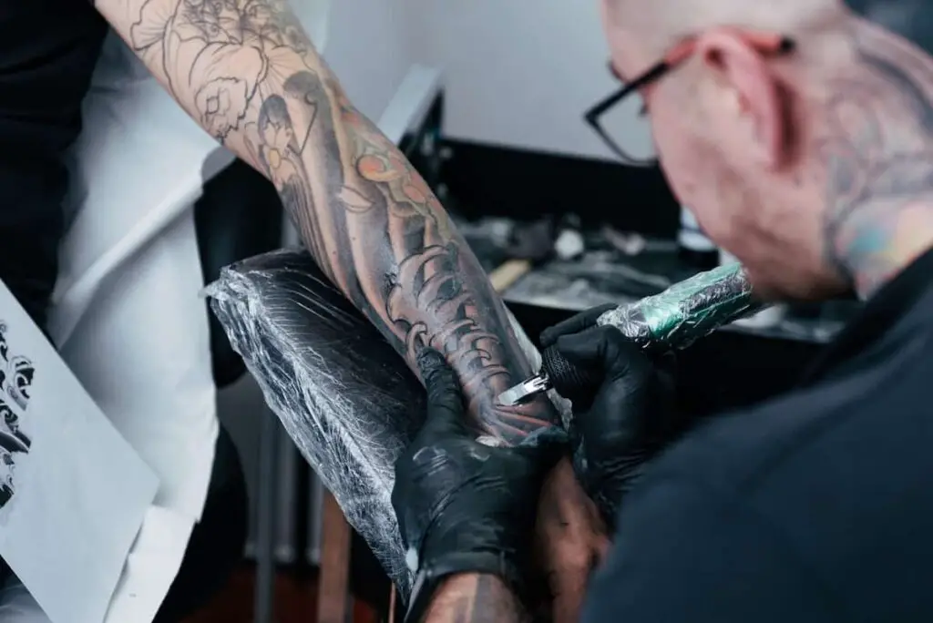 A tattoo artist working on a client's arm resting on an arm rest.
