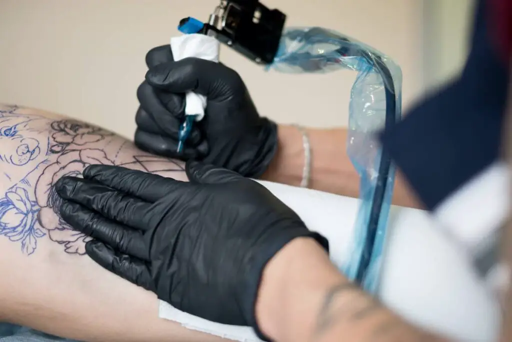 A tattoo artist using an electric corded tattoo gun.