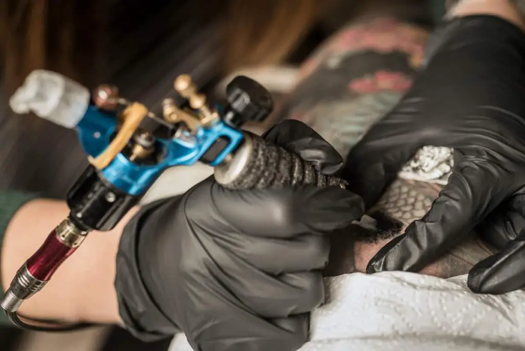 Closeup of a tattoo artist working with an electric corded tattoo gun.